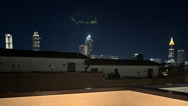 Un espace extérieur aménagé avec des sièges et un foyer, entouré de chaises, offrant une vue sur le paysage urbain illuminé la nuit.