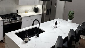 Une cuisine moderne avec des meubles blancs, une cuisinière en acier inoxydable, des suspensions noires et un îlot central doté de tabourets de bar.