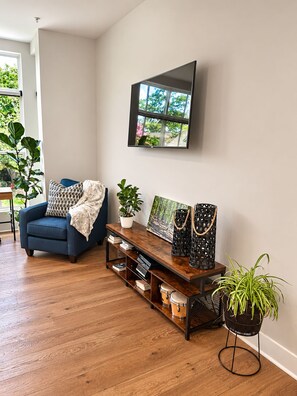 A living room with a blue sofa, a coffee table with decorative items, a mounted TV, and a potted plant. - Atlanta Skyline Rooftop, Fire Pit, BeltLine and Garage (Atlanta)