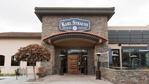 The exterior of Karl Strauss Brewing Company with a stone facade, a wooden entrance, and outdoor seating visible through large windows.