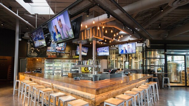 A bar area with multiple screens, stools, and a bar counter.