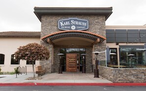 The exterior of Karl Strauss Brewing Company with a stone facade, a wooden entrance, and outdoor seating visible through large windows. - Grand Pacific Palisades Resort 2 Bedroom, 2 Bath Suite (Carlsbad)