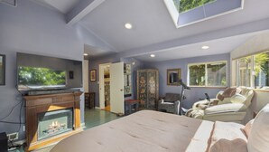 Un dormitorio con una cama grande, chimenea, televisor y tragaluz.
