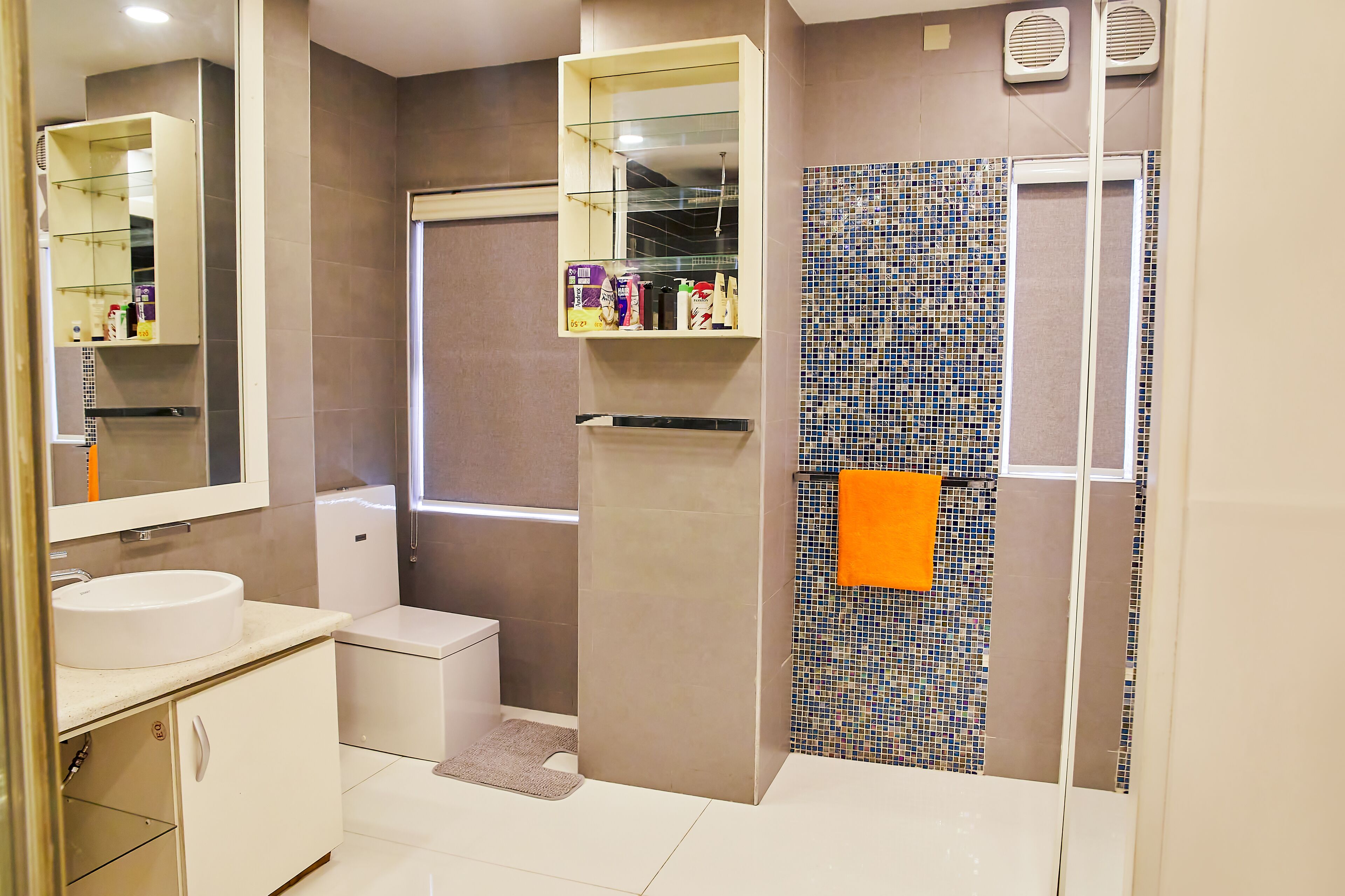 Een moderne badkamer met een witte wastafel, toilet, douche met glazen deur en een betegelde muur met mozaïekpatroon.