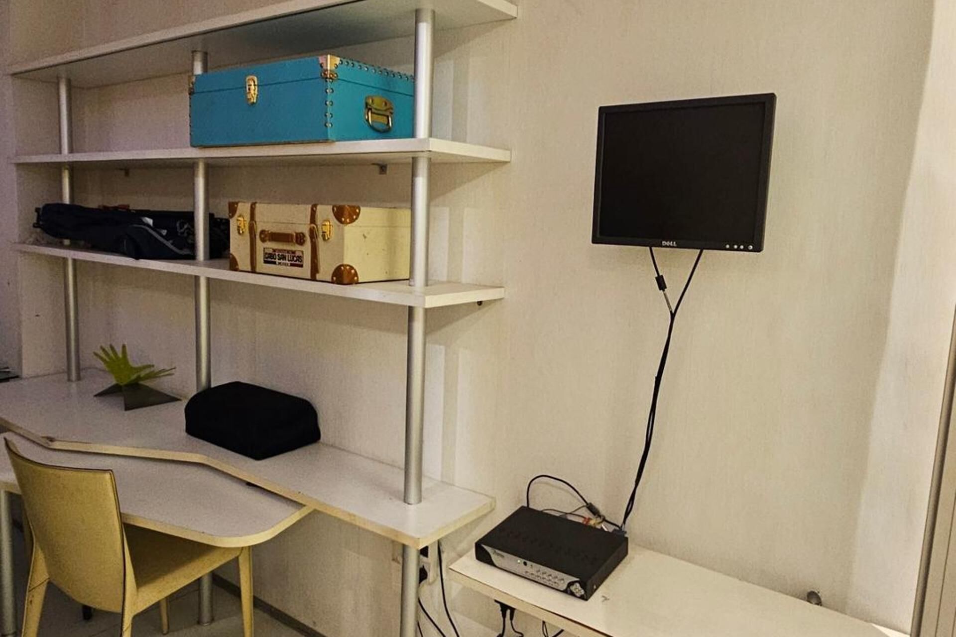 A room with a white desk, a computer monitor, and a shelf with storage boxes.