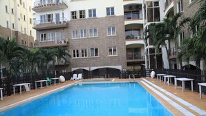 Une piscine dotée d’une plage carrelée, entourée d’une clôture et jouxtant un immeuble à plusieurs étages avec des balcons.