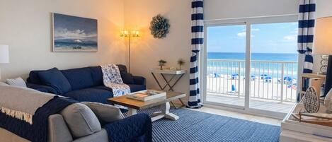 A living room with a sofa, a coffee table, a lamp, and a view of the beach through a sliding door.