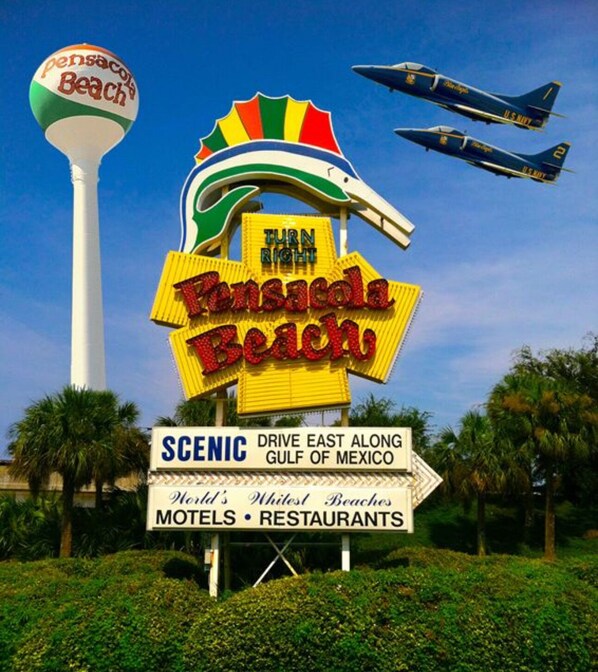 A Pensacola Beach sign with a large, colorful logo and a directional arrow.