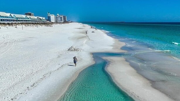 Een strand met helder turquoise water, een zandstrand en een pier in de verte.