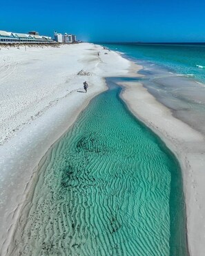A beach with clear turquoise water, a sandy shore, and a pier in the background.