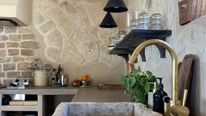 Una cocina rústica con un lavabo de piedra, un estante de madera con frascos de vidrio y una lámpara colgante.