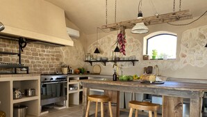 Una cocina rústica con pared de piedra, taburetes de madera, una isla grande y una lámpara colgante.