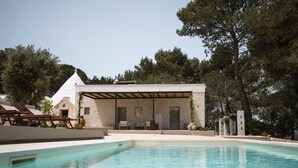 Un área moderna junto a la piscina con una piscina cristalina, sillas de descanso y una zona de estar cubierta.