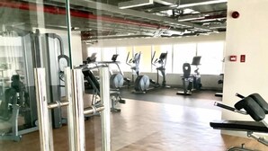 Un gimnasio con diferentes máquinas de ejercicio, un panel de vidrio y suelo de madera.