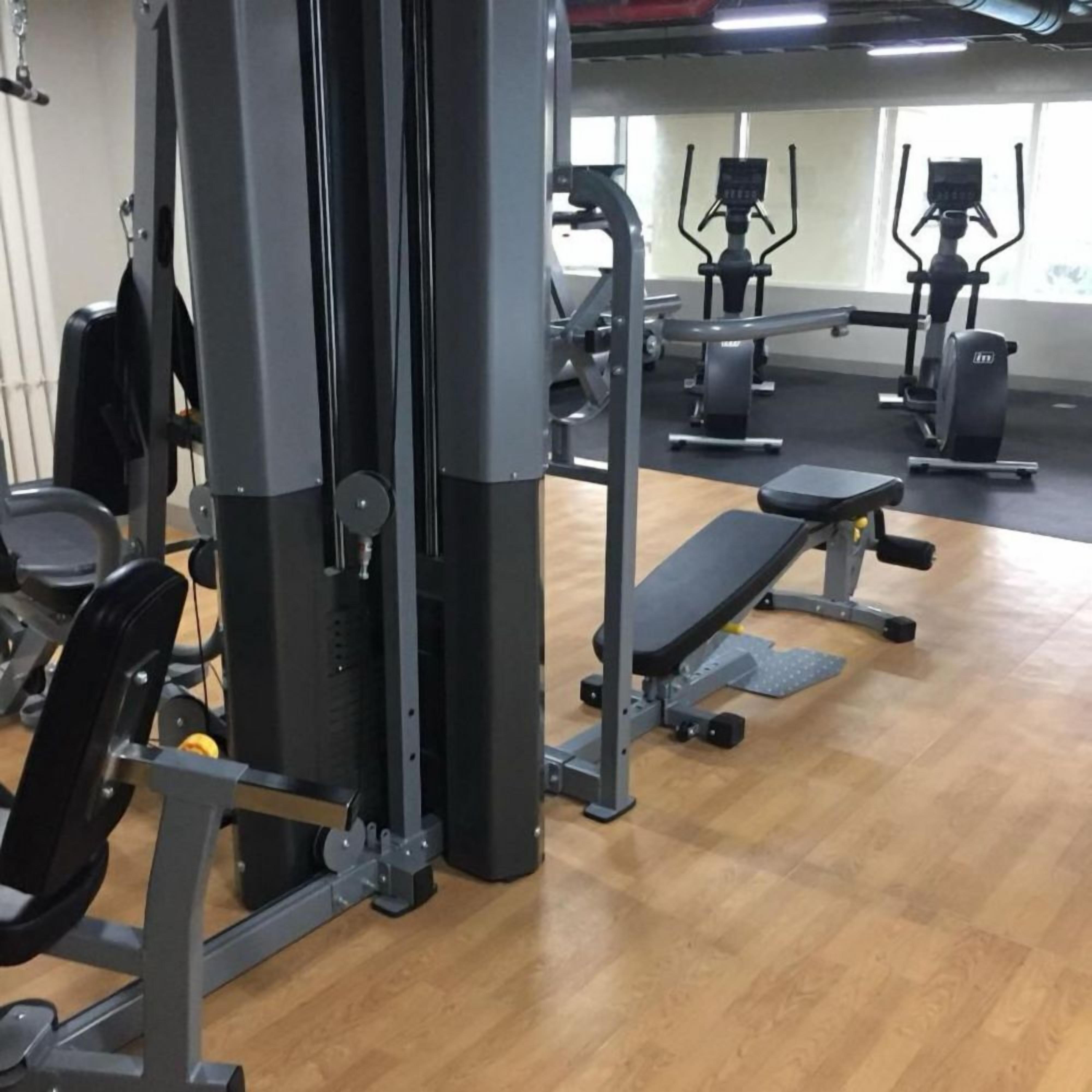 A gym with various exercise equipment, including a bench press, a squat rack, and cardio machines.