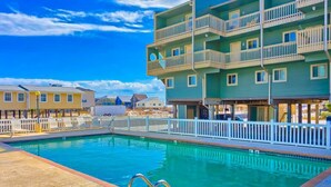 A swimming pool with a white fence and a building with balconies. - Summer House West C202 (Gulf Shores)