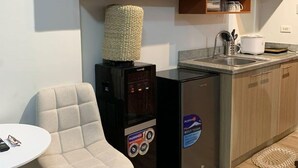 Una cocina compacta con refrigerador, cafetera y una pequeña mesa de comedor con una silla.
