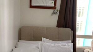 Una cama con sábanas blancas, cabecera y ventana con cortinas.