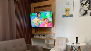 Una sala de estar con un sofá, un televisor, una pequeña mesa y una silla.