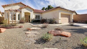 A single-story house with a tiled roof, a front garage, and a landscaped front yard with rocks and sparse vegetation. - Spacious Las Vegas Home w/ Private Pool + Hot Tub (Las Vegas)