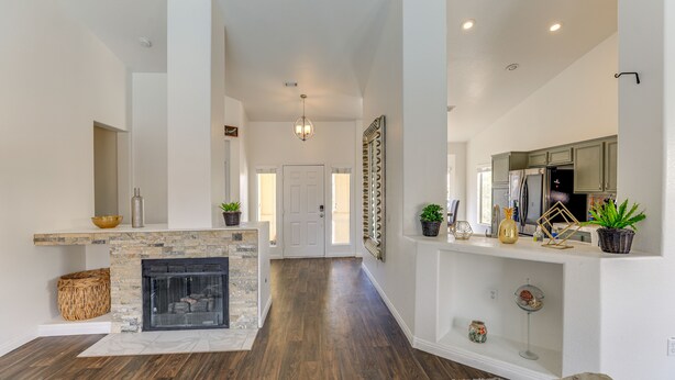 A spacious living area with a fireplace, wooden flooring, and a modern kitchen in the background. - Spacious Las Vegas Home w/ Private Pool + Hot Tub (Las Vegas)