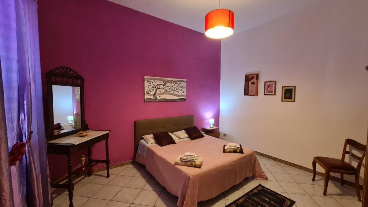 Une chambre à coucher comprenant un lit, une table de chevet, une chaise, un miroir et un mur orné de tableaux.