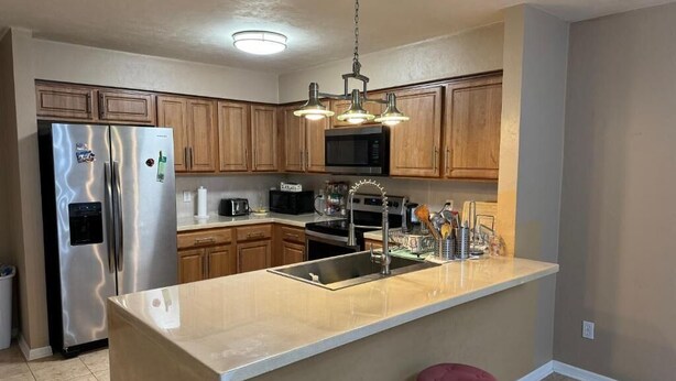 Una cocina moderna con armarios de madera, electrodomésticos de acero inoxidable, una isla central con taburetes e iluminación colgante.