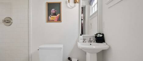 Un baño con inodoro, lavamanos y un cuadro en la pared.