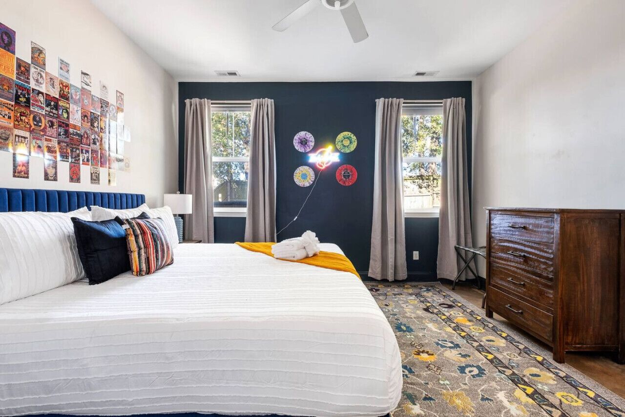 Un dormitorio con cama, cómoda, pared con carteles y ventana con cortinas.