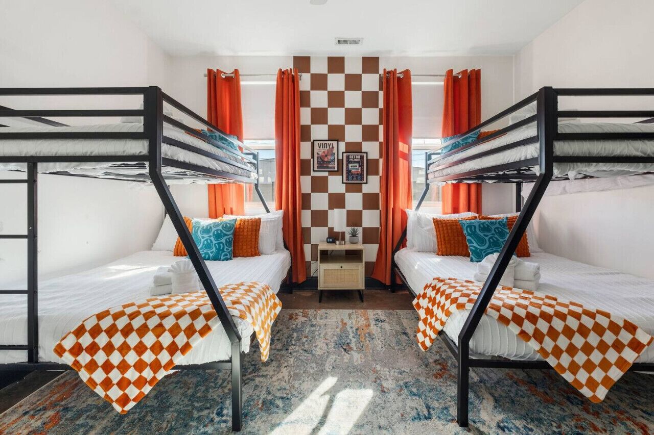 Una habitación con literas, mantas a cuadros naranja y un estampado de cuadros en la pared.