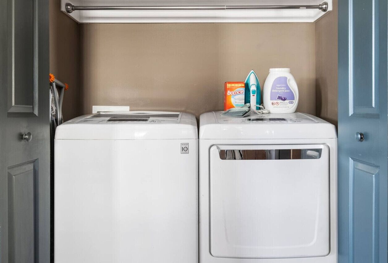 A laundry area with two washing machines and a shelf with laundry detergent and an iron.