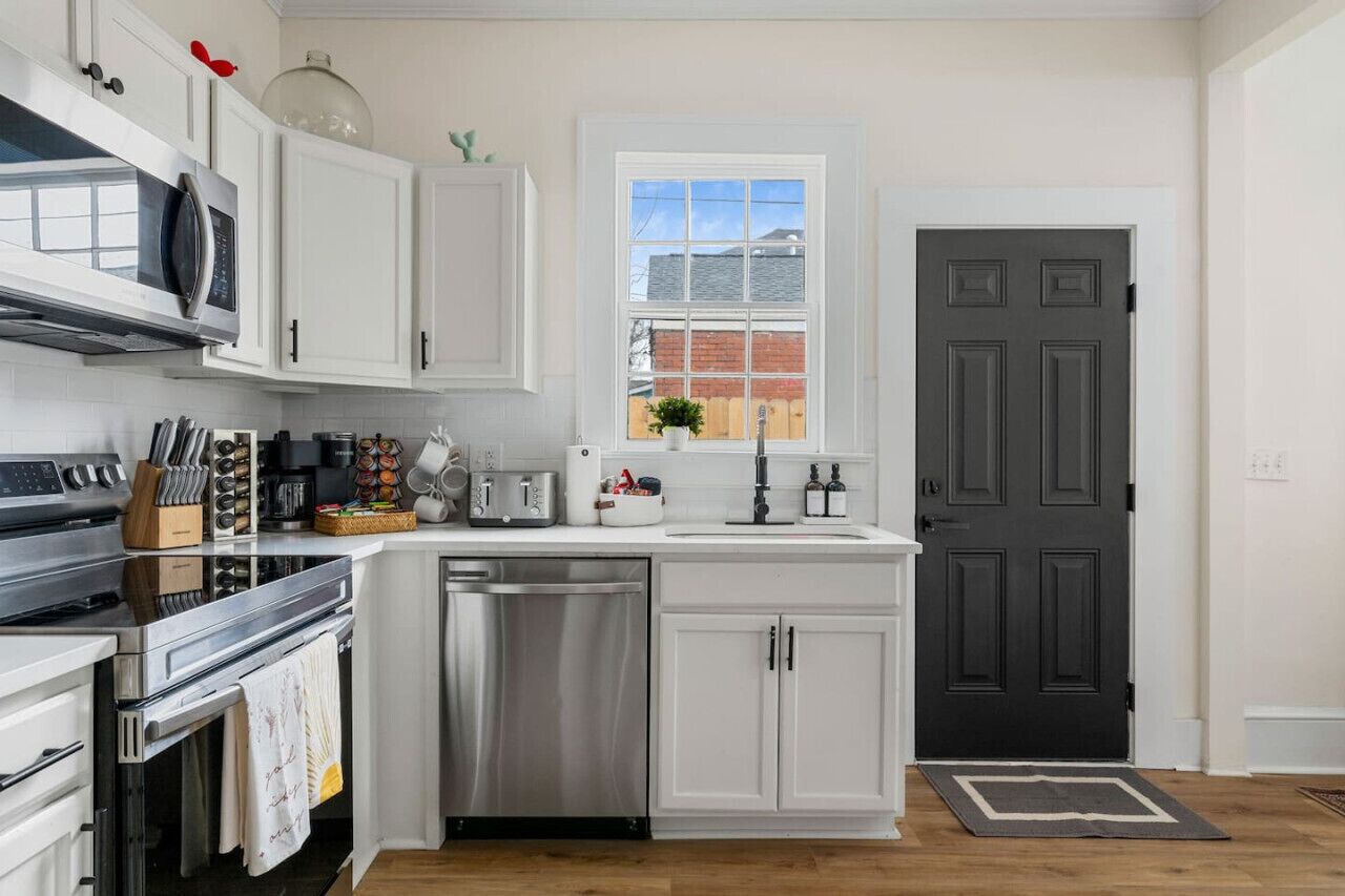 A modern kitchen with white cabinets, stainless steel appliances, and a window above the sink.