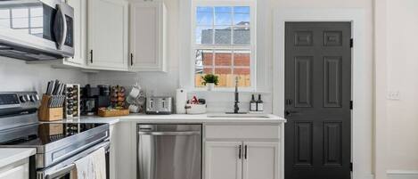 A modern kitchen with white cabinets, stainless steel appliances, and a window above the sink.