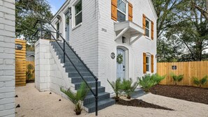 Un bâtiment blanc avec un escalier menant à l’entrée, une clôture en bois et de petites plantes dans le jardin.