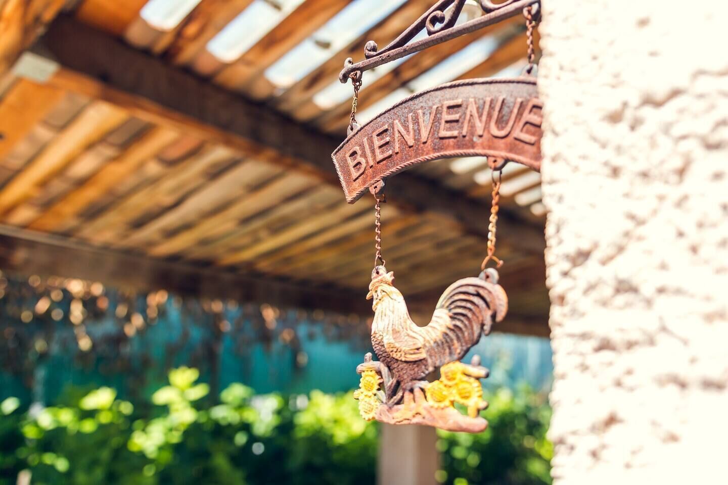 A rustic metal sign with a rooster and the word "BIENVENUE" hanging from a wooden structure.