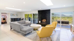 Una sala de estar moderna con chimenea, un sofá, un sillón amarillo y un comedor con vistas al exterior.