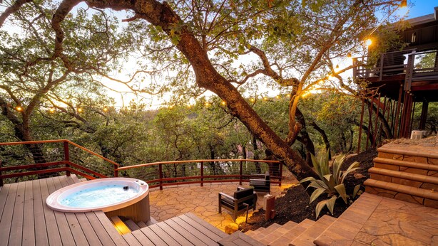 Una terraza de madera con un jacuzzi, asientos al aire libre y una escalera que lleva a un área cubierta.