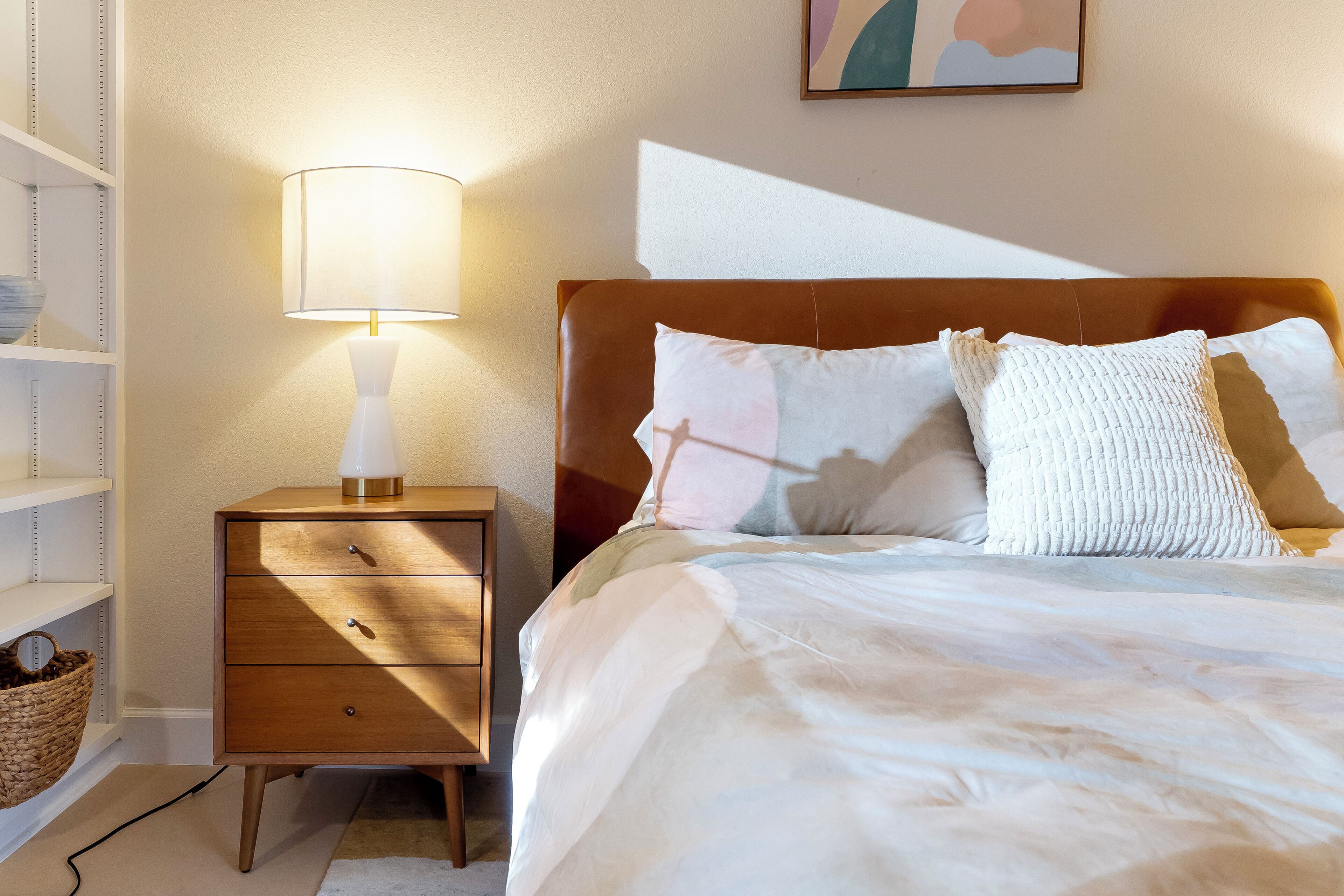 Un dormitorio ordenado con cama, lámpara de noche y mesita de noche con cajones.
