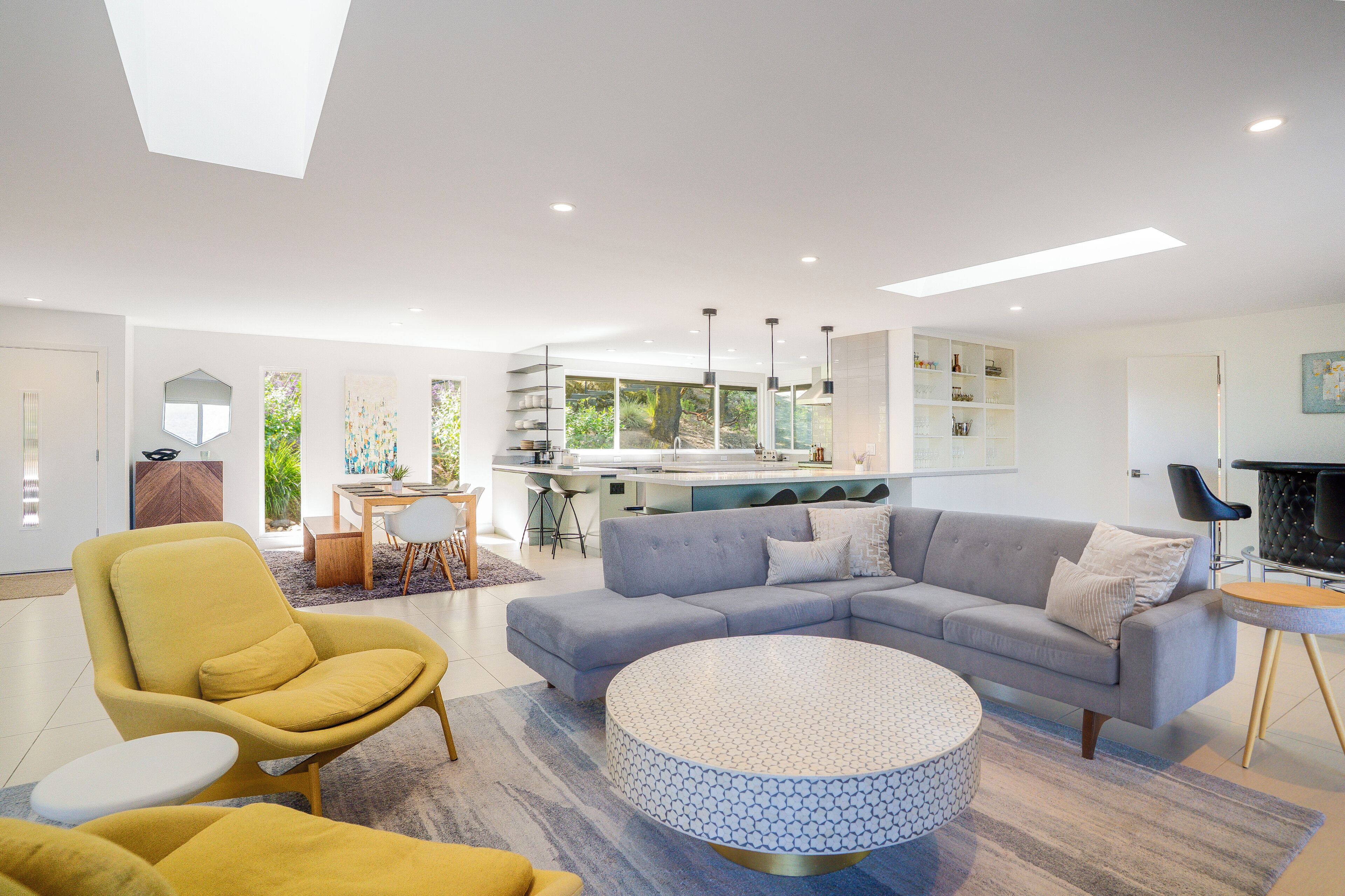 A modern living room with a sofa, armchairs, a coffee table, and a kitchen in the background.