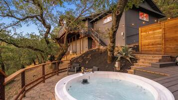 A hot tub on a wooden deck with a staircase leading to a house.