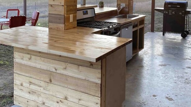 A rustic kitchen with a wooden island, pendant lights, and a view of the outdoors.