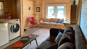A cozy cabin interior with a washing machine, a red chair, a sofa, and a dining table.