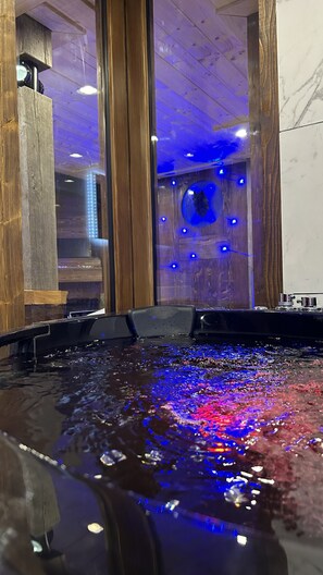 A room with a large window, wooden beams, and a water feature with blue lighting. - Chalet de Montagne Avec Balnéo (La Bresse)