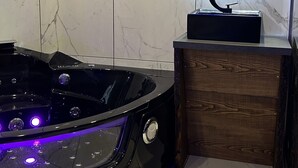 Une salle de bain moderne avec un jacuzzi noir, un meuble-lavabo en bois et un mur recouvert de carreaux de marbre.