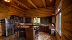 A log cabin kitchen with a central island, stainless steel appliances, and wooden cabinetry.