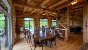 A spacious log cabin with a large dining table, wooden floors, and a spiral staircase.