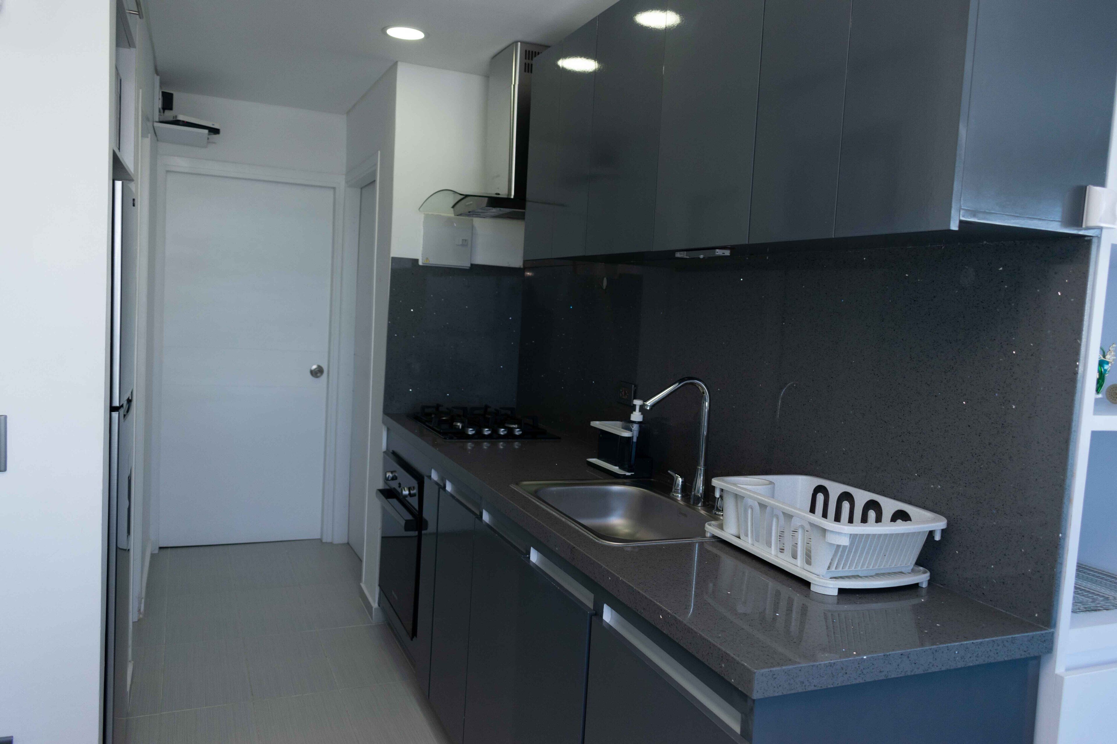 A modern kitchen with dark cabinets, a stainless steel sink, and a white countertop.