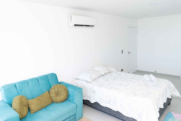 A bedroom with a bed, a blue sofa, and an air conditioning unit.