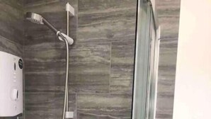 Een douche met een glazen deur, een handdouche en een bedieningspaneel aan de muur.