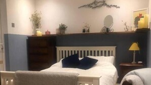 Een slaapkamer met een wit bed, een nachtkastje, een lamp en een spiegel aan de muur.